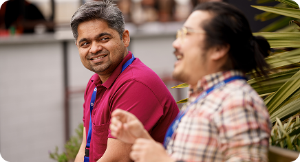 Two colleagues wearing lanyards chatting and smiling while taking a break outdoors.