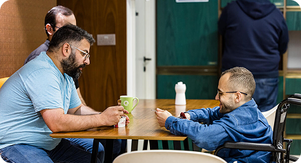 People sitting at a table in a casual indoor space, chatting and smiling, including a wheelchair user.