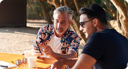 Two people sitting at an outdoor table, looking at a smartphone together.